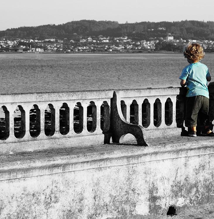 Niño mirando al mar subido en una balaustrada en la isla de La Toja, Pontevedra, Galicia