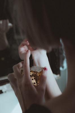 Mujer perfumándose la muñeca delante de un espejo Mujer perfumándose la muñeca delante de un espejo