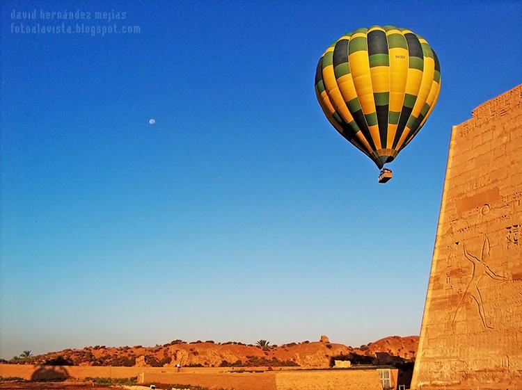 Un globo aerostático se eleva en el cielo del desierto de Egipto, muy cerca de un templo con el relieve de un faraón en la fachada, al que parece que se le ha escapado el globo de la mano o que está señalándolo