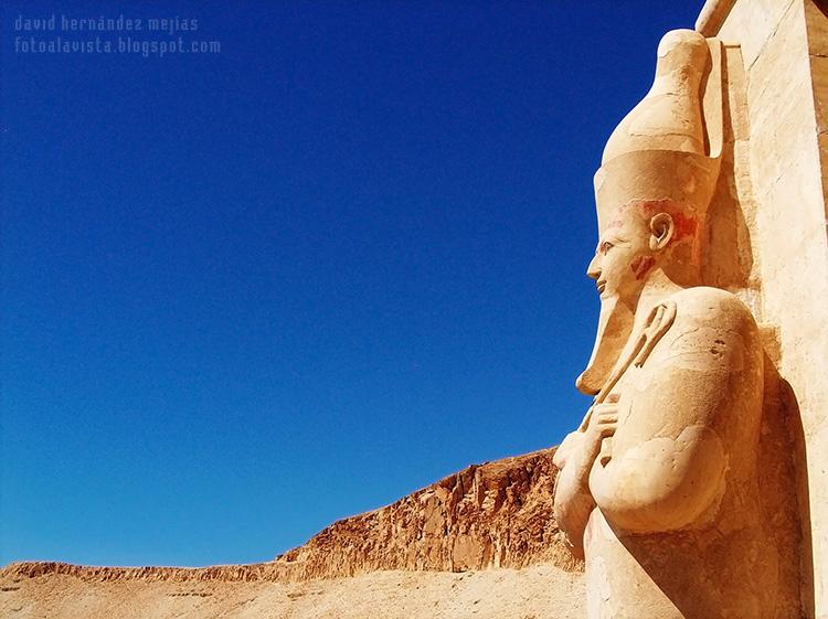 Fotografía de un escultural y colosal faraón de piedra a la entrada de un mágnífico templo, que parece tener la mirada perdida hacia el desierto de pasadas civilizaciones. Egipto