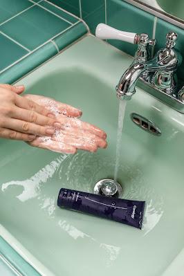 Persona emulsionando jabón con sus manos debajo del grifo del lavabo