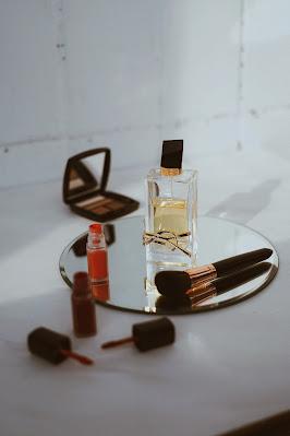 Colorete líquido en una bandeja al lado de una brocha y perfume, sobre un espejo