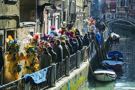 Carnaval de Venecia Una procesión de carnaval con personas vestidas con trajes brillantes a lo largo de un estrecho canal de Venecia.