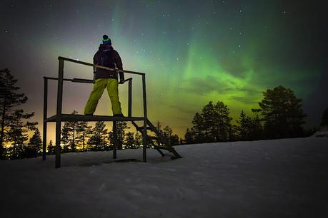 Aurora boreal en Laponia. Un hombre ve brillar la aurora boreal sobre un paisaje nevado.