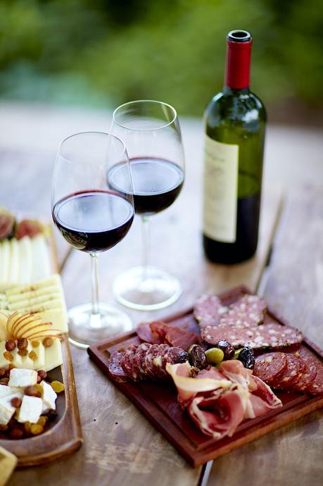 Tapas y vinos en Argentina Copas de vino tinto, queso y embutidos se sientan en una mesa de madera cerca de un viñedo.