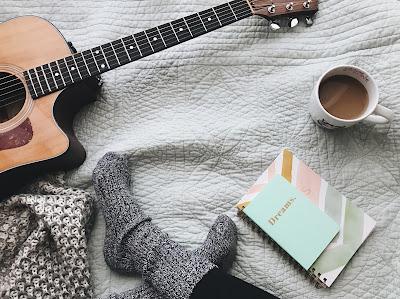 Persona sentada en el suelo con calcetines, una guitarra, cuadernos y una taza de café Persona sentada en el suelo con calcetines, una guitarra, cuadernos y una taza de café