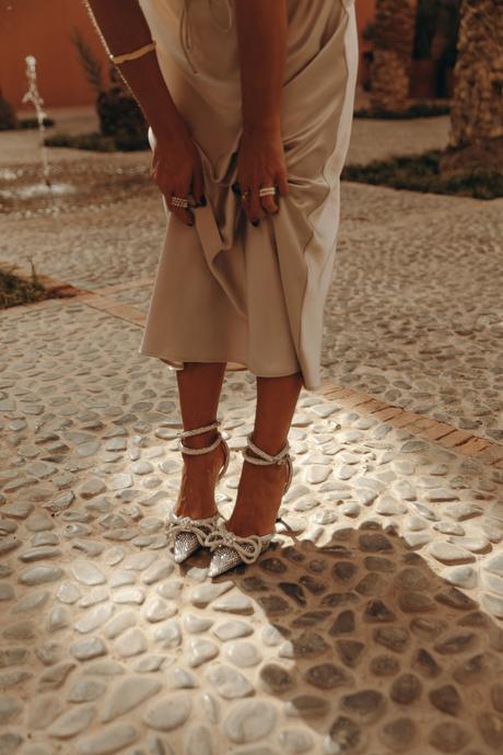 Sara from Collage Vintage wearing a satin long skirt, Mach & Mach crystal embellished pumps and maxi hoops in a palm tree garden in Marrakech