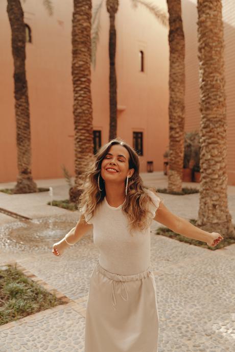 Sara from Collage Vintage wearing a satin long skirt, Mach & Mach crystal embellished pumps and maxi hoops in a palm tree garden in Marrakech