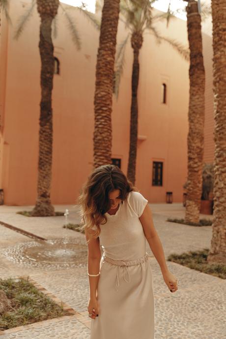 Sara from Collage Vintage wearing a satin long skirt, Mach & Mach crystal embellished pumps and maxi hoops in a palm tree garden in Marrakech