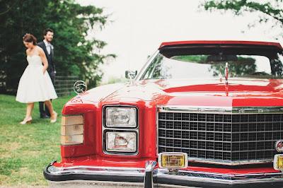 Novia con un vestido midi de aire retro junto con el novio, con un coche vintage en primer plano