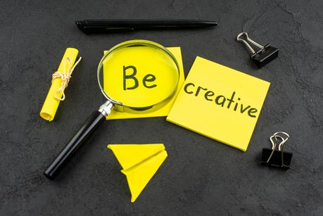 Bottom view be creative written on yellow sticky note lupa binder clips pen on dark background