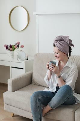Mujer tomándose un café sentada en el sofá con una toalla envolviéndole el cabello