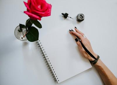 Mano femenina a punto de escribir en un cuaderno con una pluma junto a una rosa