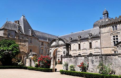 La entrada al patio del castillo con rosales rojos que bordean los muros de piedra del Château de Vayres