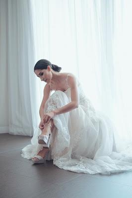 Novia sentada delante de una ventana abrochándose los zapatos