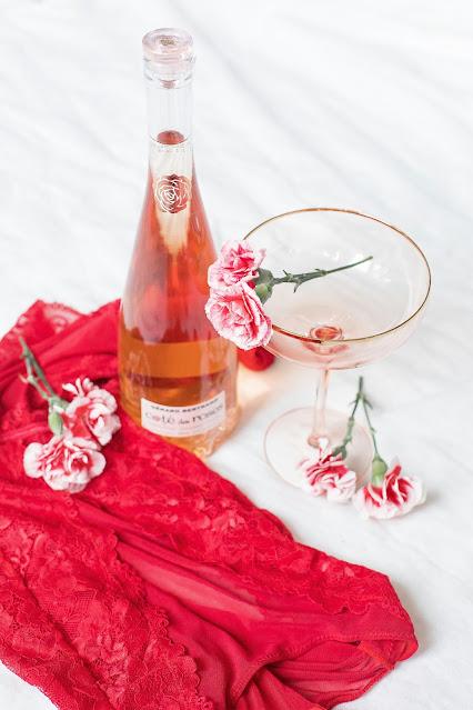 Lencería de color rojo junto con una botella pequeña de champán y flores