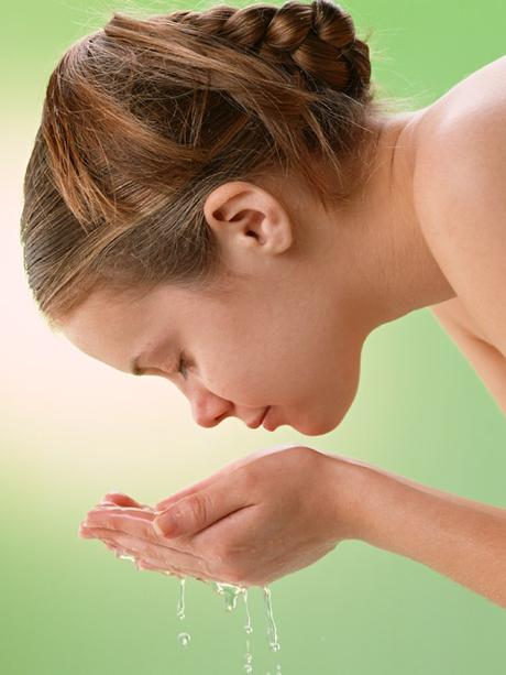Mujer lavándose la cara sobre un fondo verde Mujer lavándose la cara sobre un fondo verde