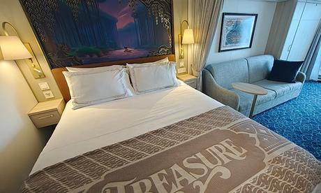 Camarote interior del crucero Disney Treasure con cama, sofá y decoración temática de Disney
