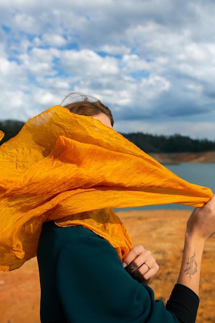 Mujer con un gran pañuelo naranja sobre el rostro y movido por el viento