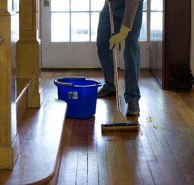 Persona limpiando un suelo de madera con un cubo de la fregona al lado