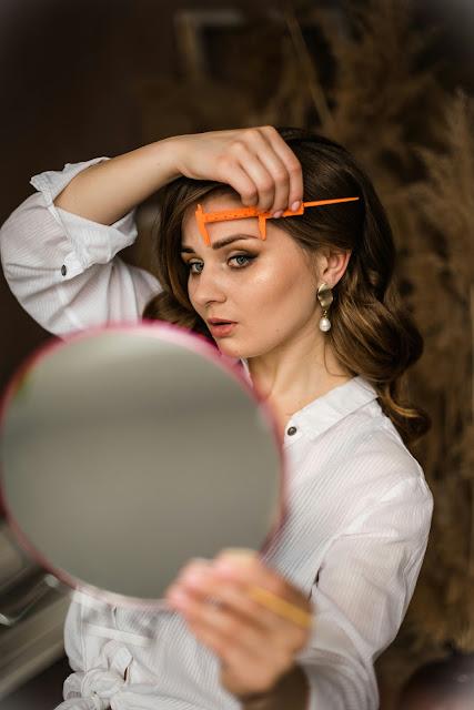 Mujer mirándose al espejo y tomando medidas de sus cejas