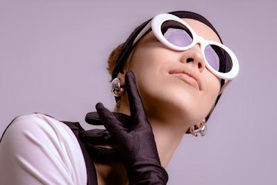 Mujer con gafas retro y una mano enguantada rozándose el rostro