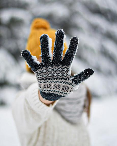 Mujer con una mano extendida, con los dedos abiertos, con un guante de lana en un paisaje invernal